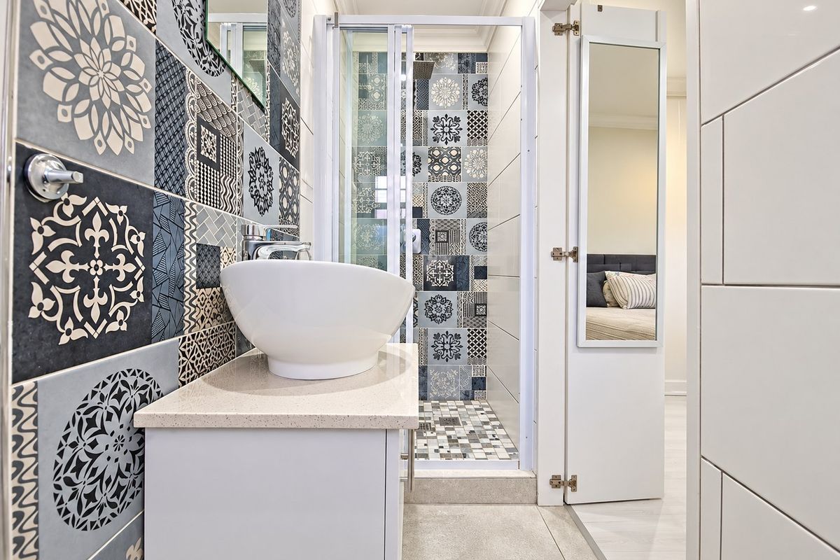 Modern bathroom featuring a stylish vessel sink on a stone vanity, a glass-enclosed shower, and decorative patterned wall tiles.