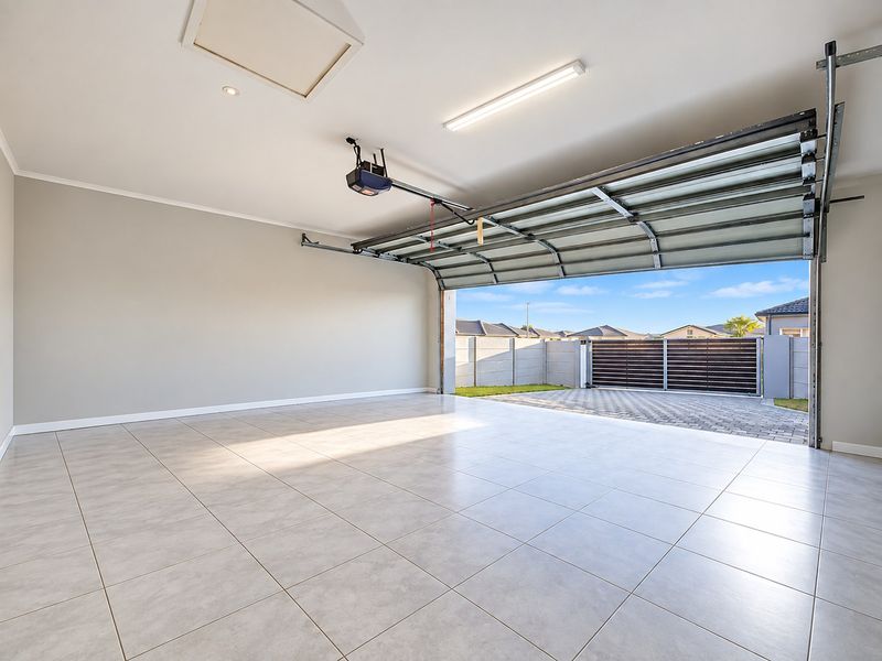A clean, spacious double garage featuring neutral tiled flooring, overhead lighting, and an automatic door mechanism, providing secure parking and additional storage space.