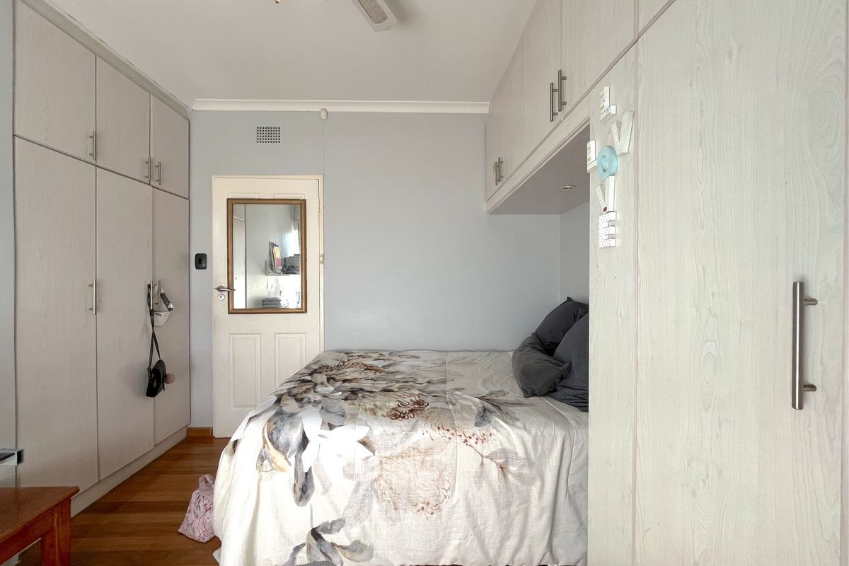 A well-maintained bedroom featuring extensive built-in cabinetry, hardwood flooring, and a ceiling fan, offering ample storage and a functional layout.