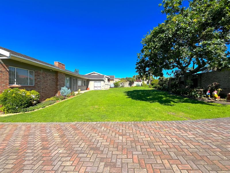Spacious rear garden featuring a well-maintained lawn, brick paving, and established trees, providing a private outdoor area adjacent to the main house structure.