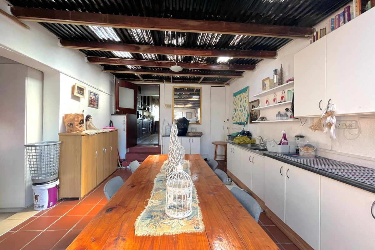 A rustic kitchen area featuring built-in cabinetry, a stainless steel sink, and an exposed beam ceiling with corrugated roofing.