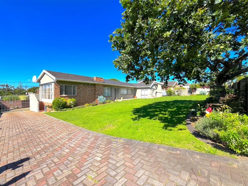 A spacious rear garden featuring a well-maintained lawn, mature tree, and brick-paved driveway leading to the rear elevation of the house.