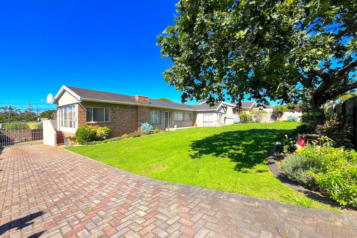 A spacious rear garden featuring a well-maintained lawn, mature tree, and brick-paved driveway leading to the rear elevation of the house.