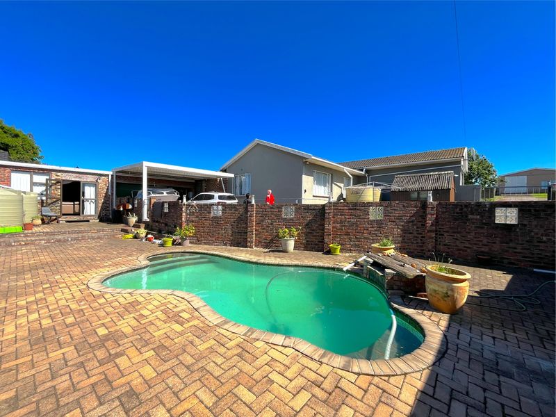 Outdoor pool area featuring a paved patio, brick boundary wall, and a covered carport structure.