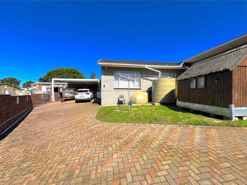 Rear exterior view featuring a paved driveway, carport, water storage tank, and a timber-clad outbuilding structure.