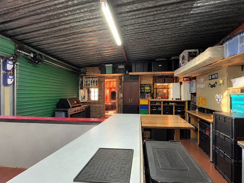 A functional garage space featuring a corrugated metal ceiling, roller shutter door, and built-in storage cabinetry, suitable for workshop or utility use.