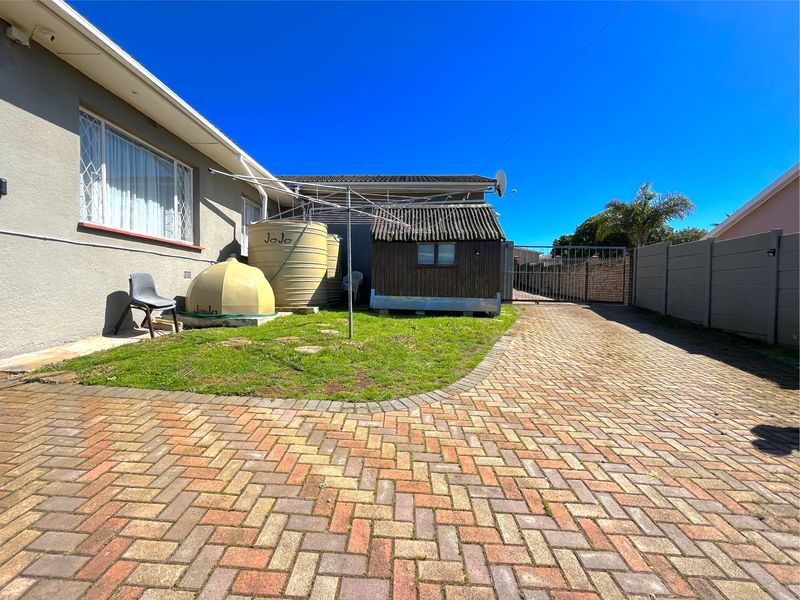 Rear exterior area featuring a paved driveway, lawn, water storage tanks, and a timber garden shed enclosed by precast walling.
