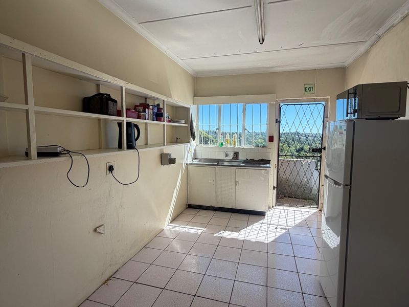 A functional scullery area featuring tiled flooring, built-in wall shelving, a stainless steel sink, and direct access to an exterior door with a security gate.