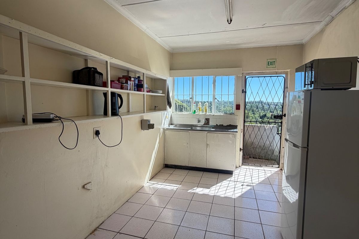 A functional scullery area featuring tiled flooring, built-in wall shelving, a stainless steel sink, and direct access to an exterior door with a security gate.