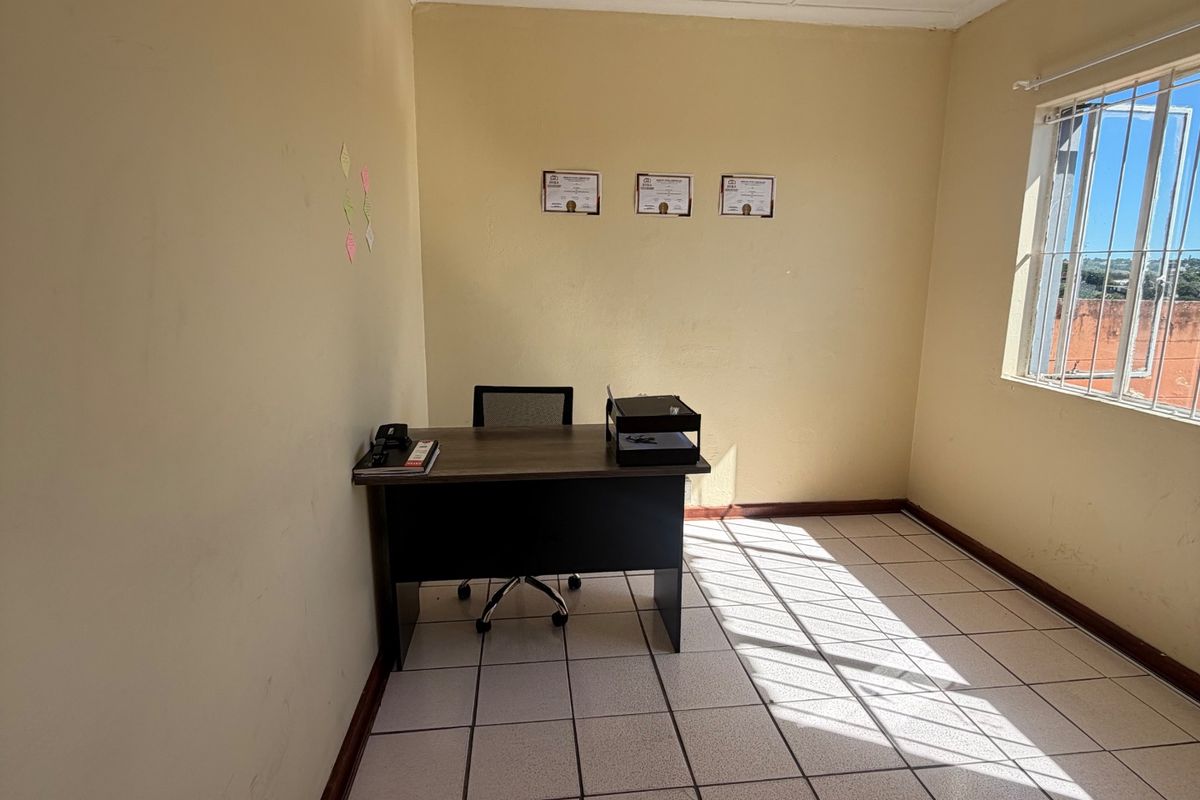A functional office space featuring ceramic floor tiles, neutral wall finishes, and a window equipped with security bars, providing natural light.
