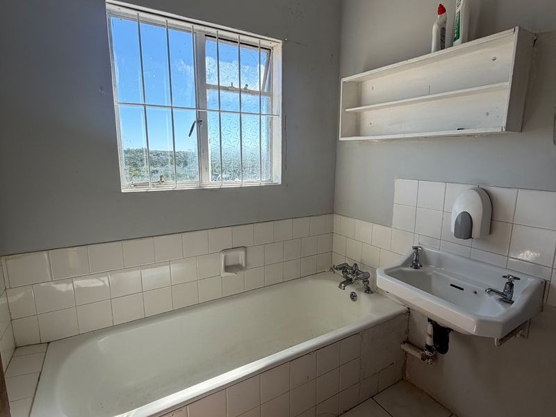 A functional bathroom featuring a built-in bathtub, wall-mounted basin, and tiled finishes, requiring cosmetic updates to improve its overall condition and appeal.