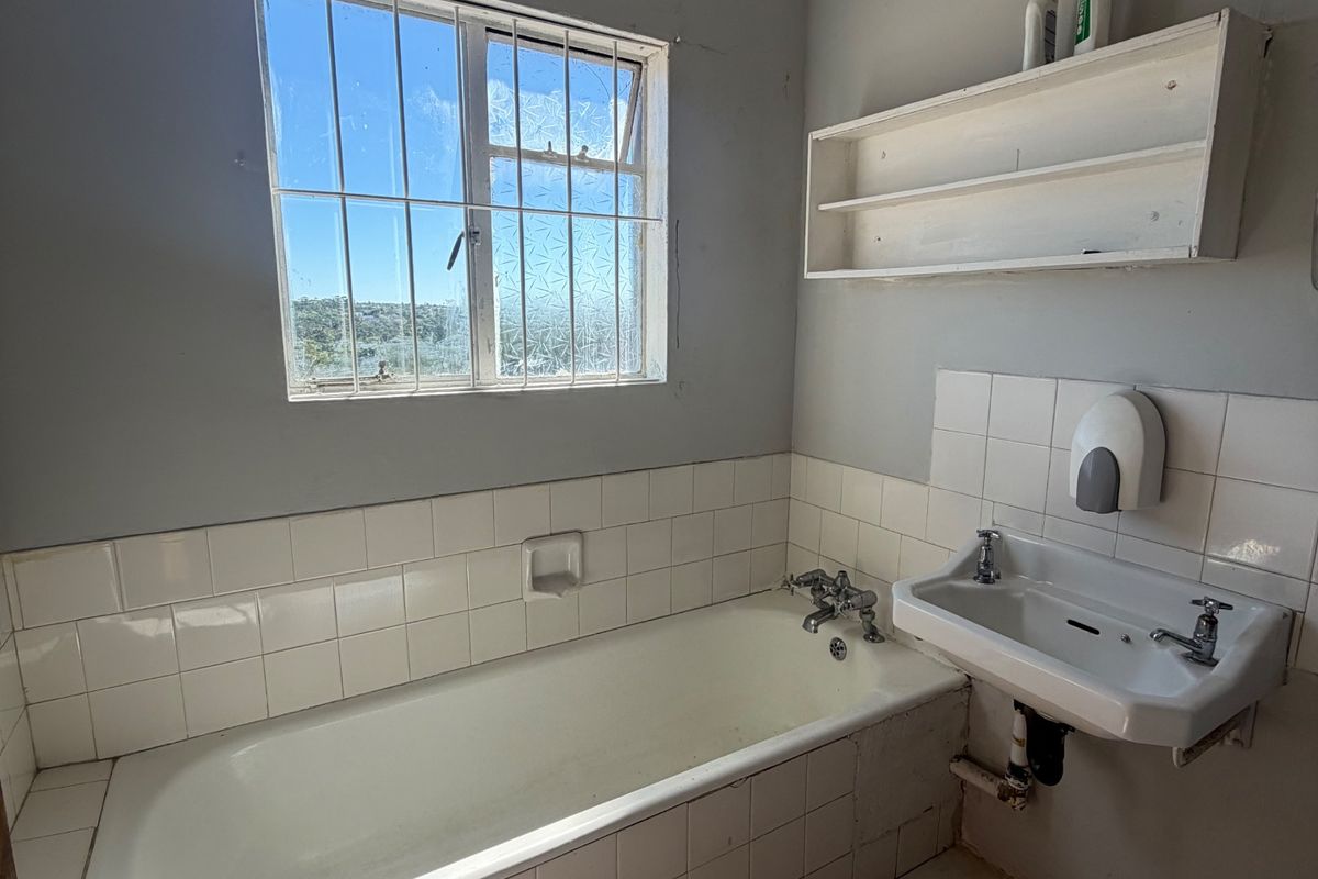 A functional bathroom featuring a built-in bathtub, wall-mounted basin, and tiled finishes, requiring cosmetic updates to improve its overall condition and appeal.