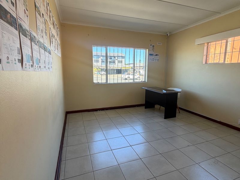 A vacant office space featuring tiled flooring, security bars on windows, and a drop ceiling, suitable for a professional workspace or commercial use.