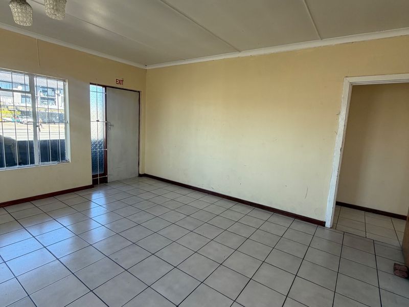 An empty, open-plan commercial space featuring neutral tiled flooring, security window bars, and a simple ceiling light fixture, ready for custom fit-out.
