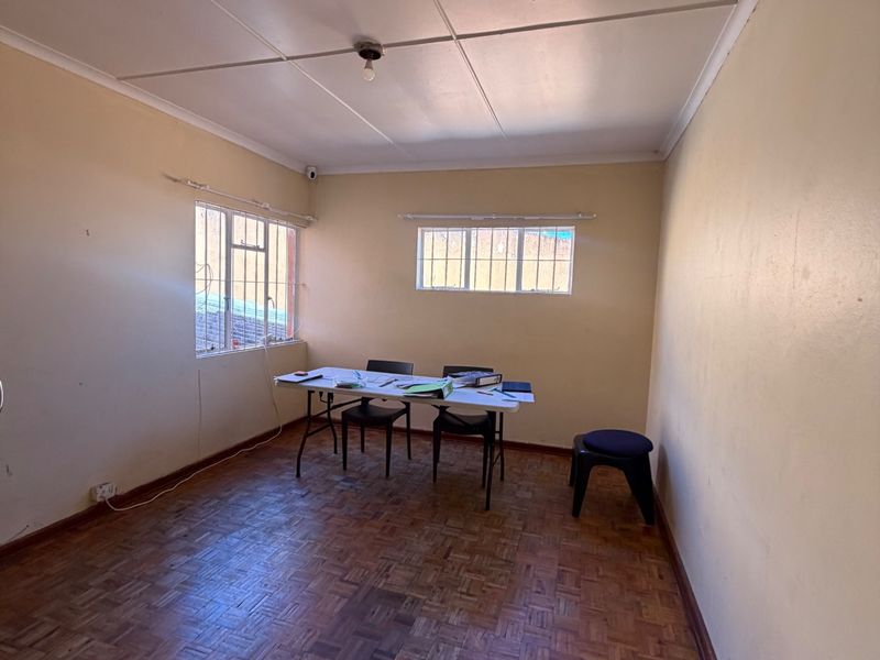 A functional office space featuring traditional parquet flooring, dual windows with security bars, and a coved ceiling, suitable for a professional workspace.