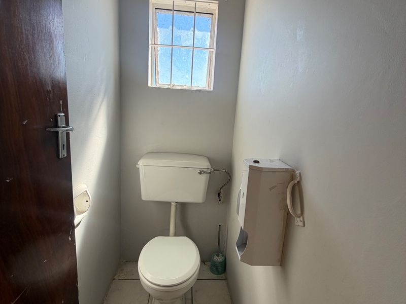 A compact commercial restroom featuring a standard toilet, tiled flooring, and a small window with security bars.