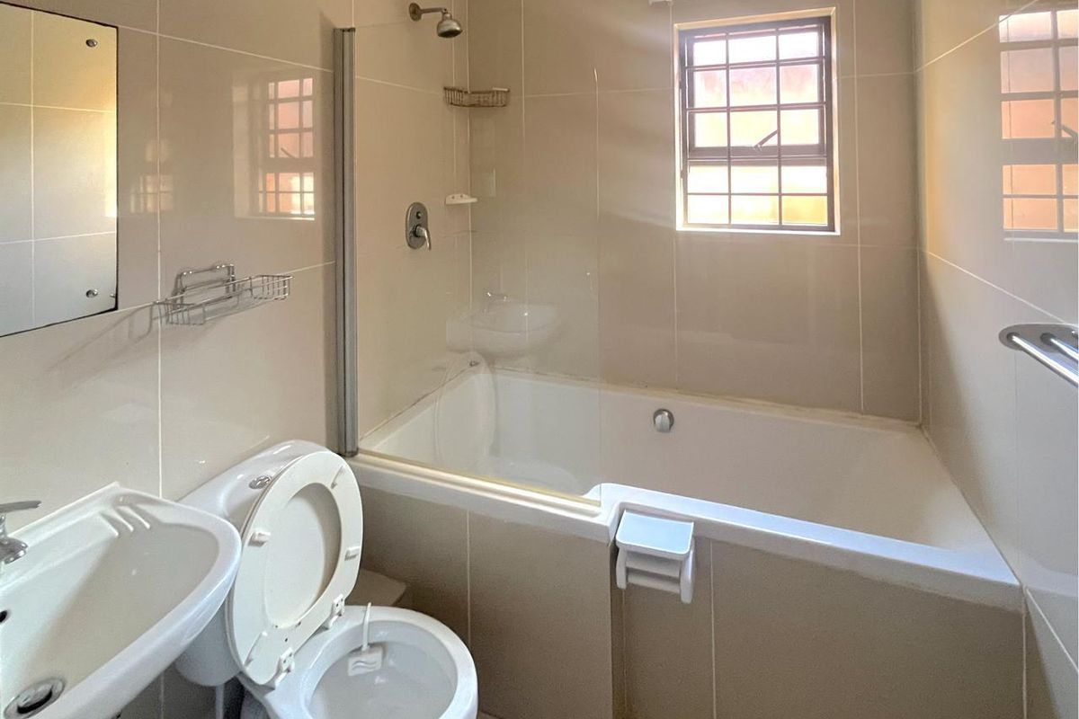 A clean, neutral-toned bathroom featuring a combined bathtub and shower, pedestal basin, and tiled finishes, offering a functional and well-maintained space.