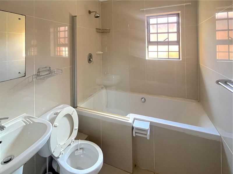 A clean, neutral-toned bathroom featuring a combined bathtub and shower, pedestal basin, and tiled finishes, offering a functional and well-maintained space.