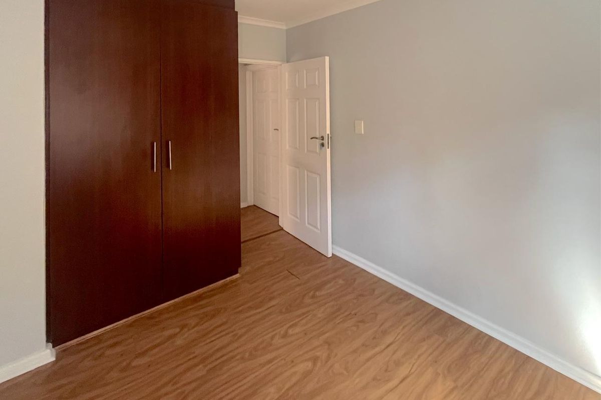 A vacant bedroom featuring laminate flooring and a dark wood built-in wardrobe, offering a clean and neutral space ready for personalization.