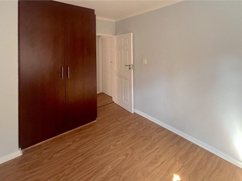 A vacant bedroom featuring laminate flooring and a dark wood built-in wardrobe, offering a clean and neutral space ready for personalization.