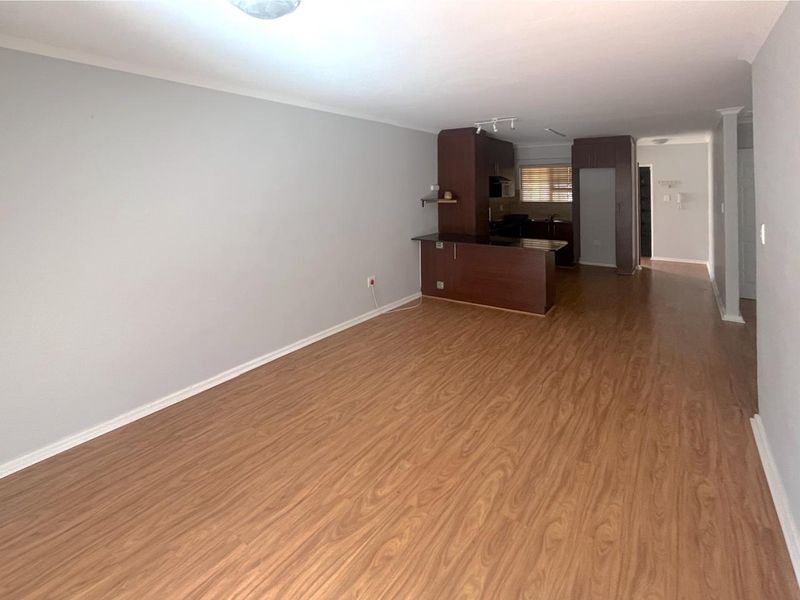 Spacious open-plan living area featuring laminate flooring and a functional kitchen with built-in cabinetry and a breakfast bar.