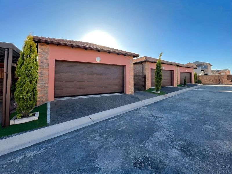 A row of townhouse garages featuring brick and plaster facades, tiled roofs, and paved driveways in a well-maintained residential complex.
