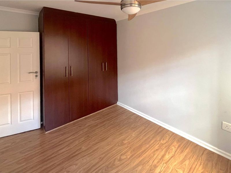 A clean, empty bedroom featuring dark wood built-in cupboards, laminate flooring, and a ceiling fan, offering a neutral space ready for personalization.
