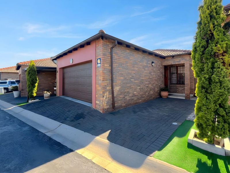 Front elevation of a townhouse featuring a brick facade, tiled roof, double garage, and paved driveway with a secure entrance.