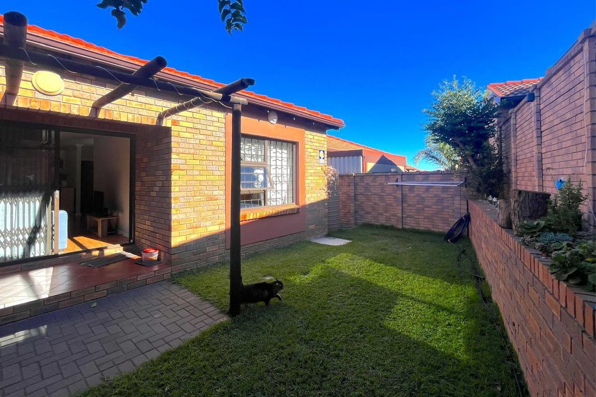 Rear view of the townhouse featuring a brick facade, a paved patio area with a timber pergola, and a private enclosed garden with brick walls.