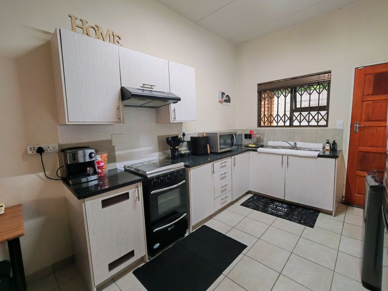 Functional kitchen featuring light wood-look cabinetry, granite countertops, a freestanding oven with extractor, and a double sink with security-grilled window.