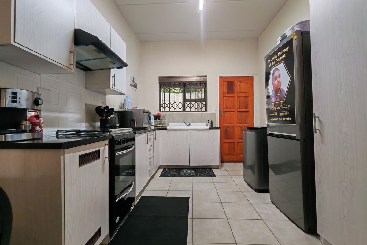 A functional kitchen featuring built-in cabinetry, a stove with extractor fan, double sink, and tiled flooring with direct access to an exterior door.