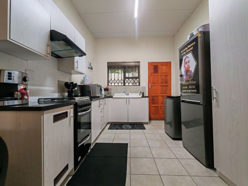 A functional kitchen featuring built-in cabinetry, a stove with extractor fan, double sink, and tiled flooring with direct access to an exterior door.