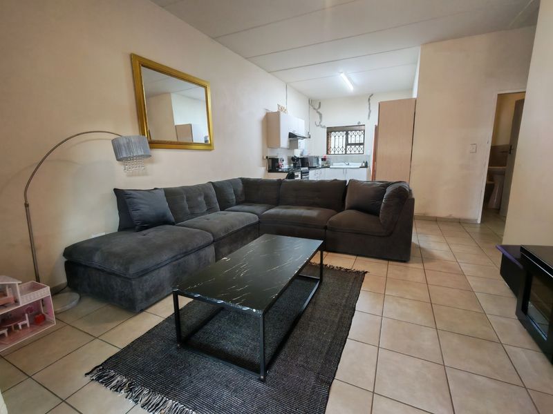 Open-plan living area featuring tiled floors and an adjoining kitchen. The space shows signs of wear, including visible wall cracks and dated finishes.