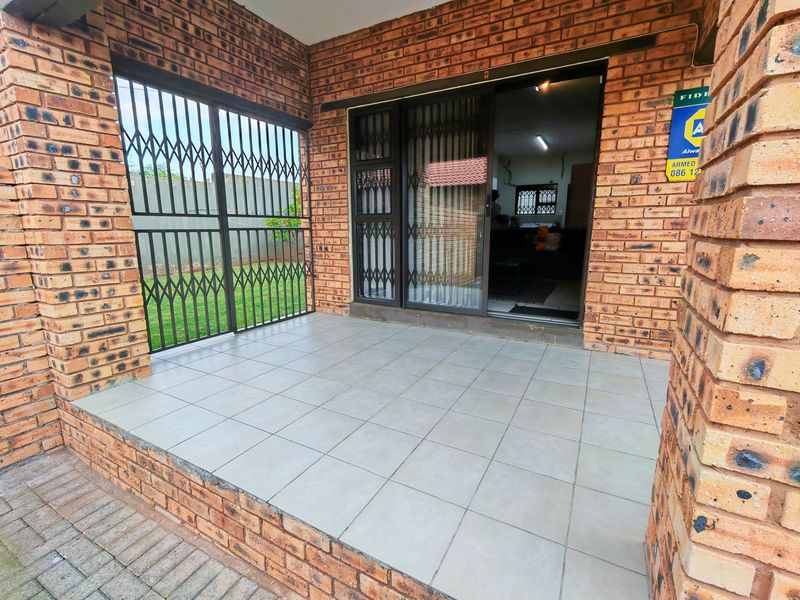 Covered patio area featuring face brick walls, tiled flooring, and a sliding glass door with security gate access.