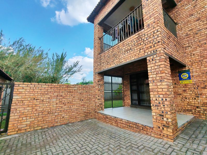 Rear view of a double-story face brick apartment featuring a ground-floor tiled patio, upper-level balcony, and a private paved courtyard with boundary walling.