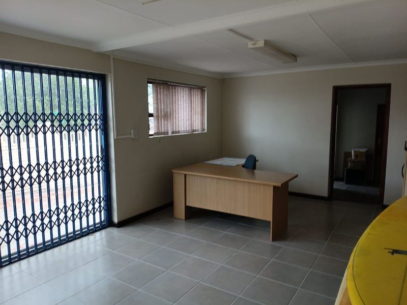 A functional commercial office space featuring tiled flooring, secure metal gate access, and neutral wall finishes, suitable for a professional work environment.
