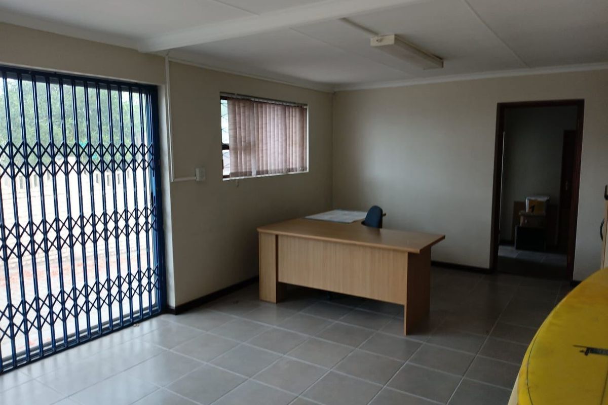 A functional commercial office space featuring tiled flooring, secure metal gate access, and neutral wall finishes, suitable for a professional work environment.