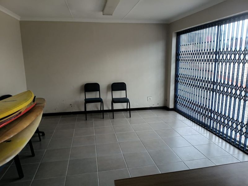 Commercial office space featuring tiled flooring, neutral walls, and a secure metal gate covering the window area.