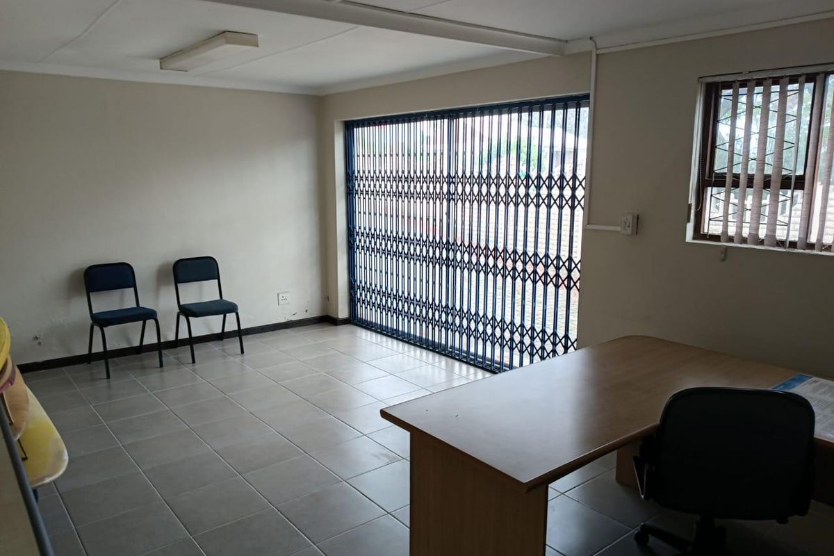 A functional commercial office space featuring tiled flooring, a secure sliding gate, and natural light through a window with security bars.