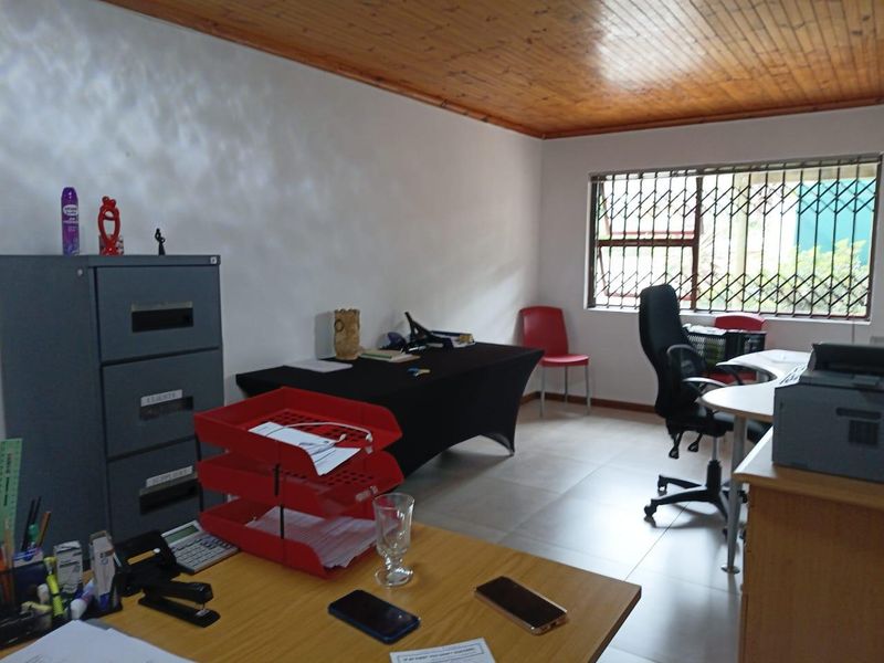 A functional office space featuring tiled flooring, a timber-clad ceiling, and windows fitted with security bars.