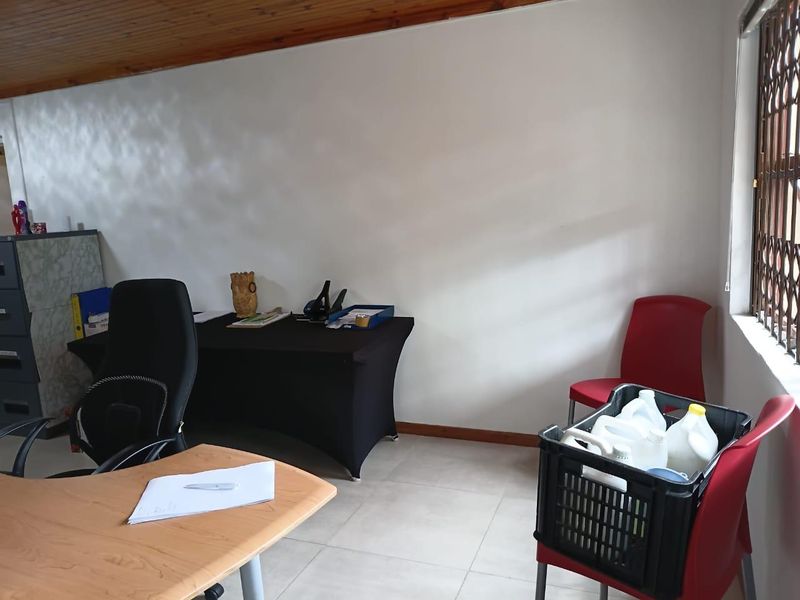A functional office space featuring tiled flooring and a timber ceiling, equipped with a security gate on the window.