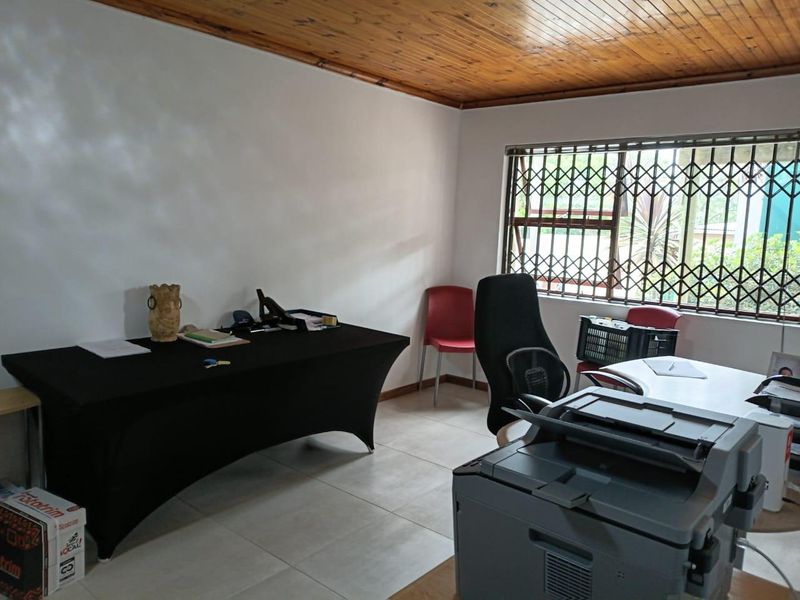 A functional office space featuring tiled flooring, a timber ceiling, and a window fitted with a security gate.
