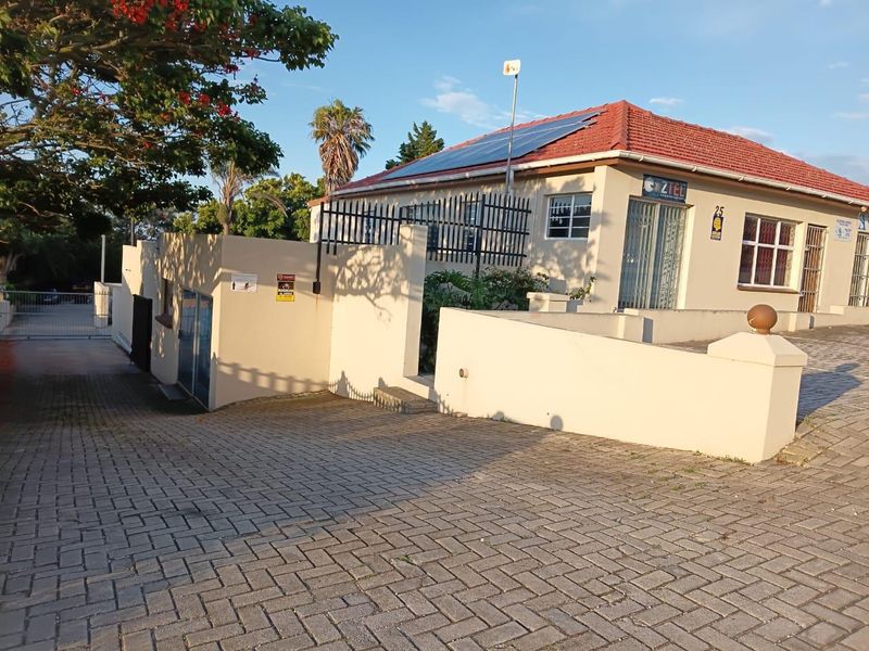 Front exterior view of a commercial property featuring a paved driveway, perimeter wall, security gate, and roof-mounted solar panels.