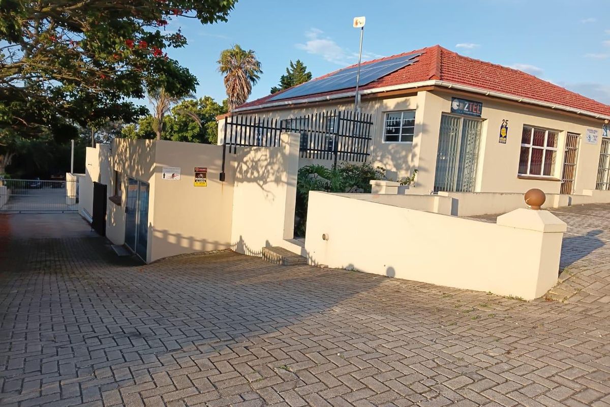 Front exterior view of a commercial property featuring a paved driveway, perimeter wall, security gate, and roof-mounted solar panels.