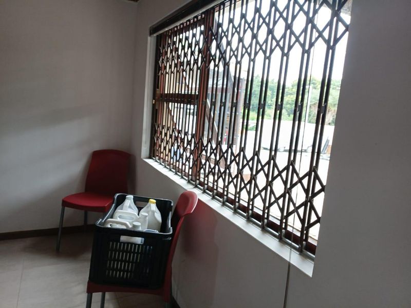 A simple office space featuring tiled flooring and a window secured with a metal security gate.