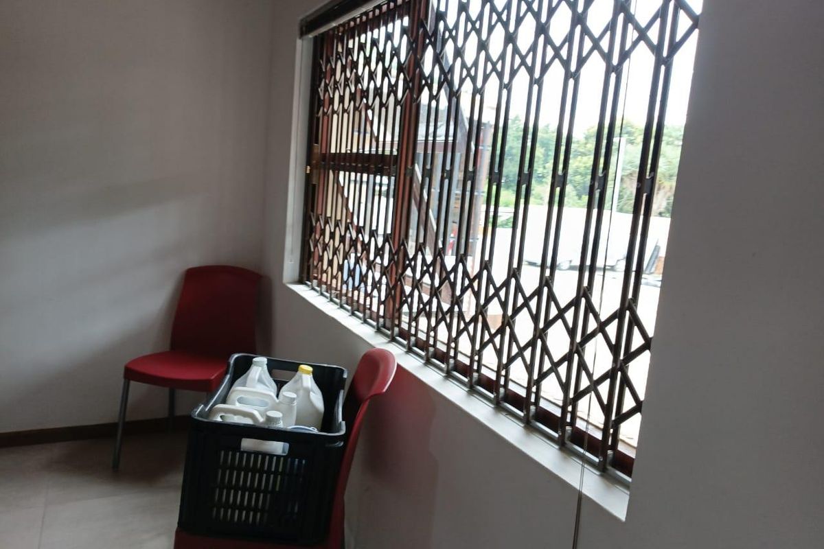 A simple office space featuring tiled flooring and a window secured with a metal security gate.