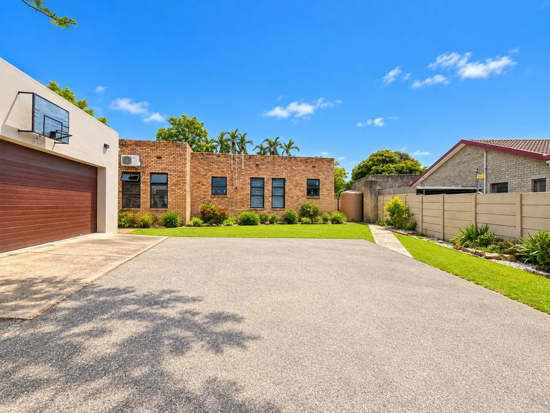 Front view of the property featuring a spacious asphalt driveway, brick exterior facade, attached garage, and a well-maintained garden area with perimeter walling.
