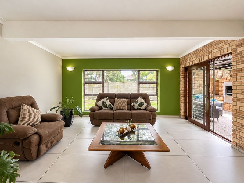Spacious living room featuring large format floor tiles, an exposed brick feature wall, and sliding glass doors providing seamless access to the outdoor patio area.