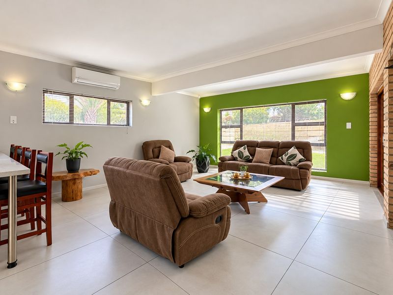 Spacious open-plan living area featuring modern tiled flooring, a brick feature wall, and split-system air conditioning with ample natural light.