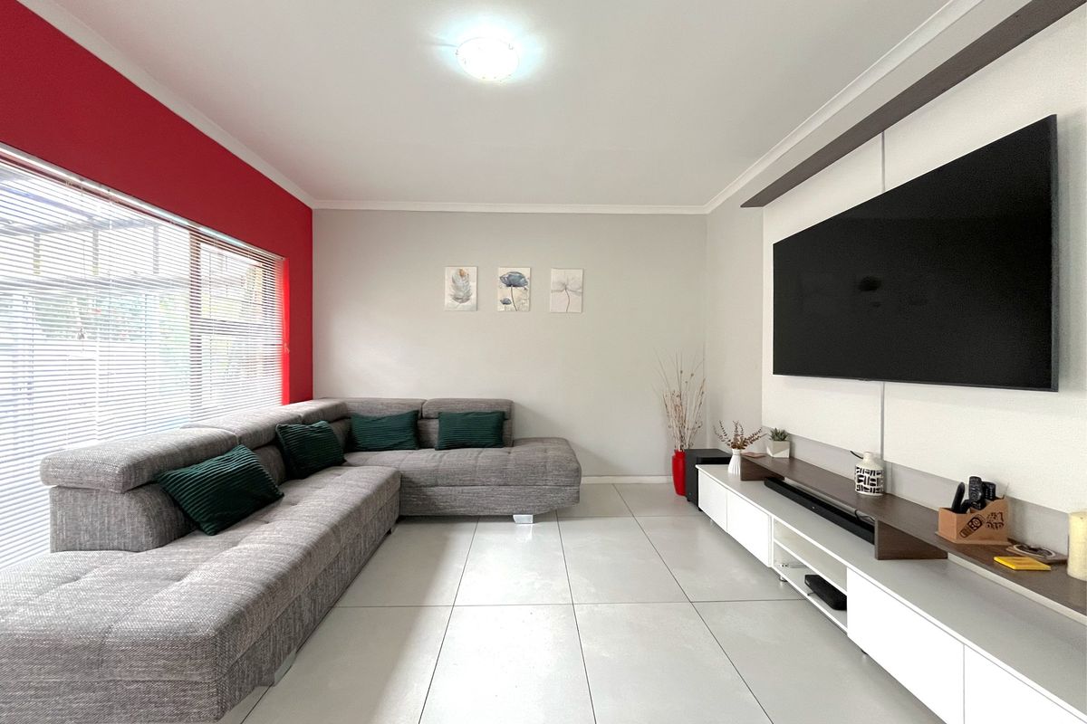 A bright and modern living room featuring large format floor tiles, a feature wall, and integrated window blinds.